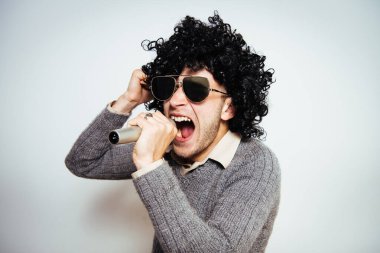 Peruklu ve güneş gözlüklü bir adam mikrofona şarkı söylüyor..