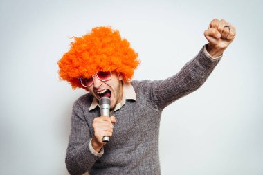 Peruklu ve güneş gözlüklü bir adam mikrofona şarkı söylüyor..