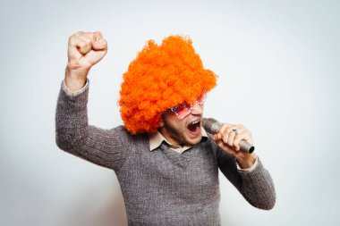 Peruklu ve güneş gözlüklü bir adam mikrofona şarkı söylüyor..