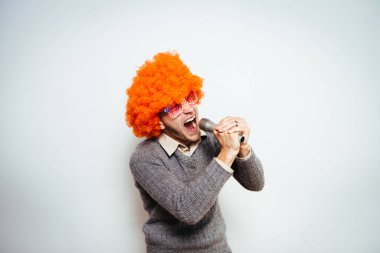 Peruklu ve güneş gözlüklü bir adam mikrofona şarkı söylüyor..