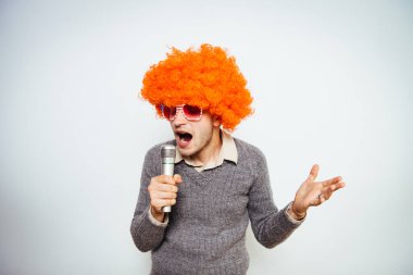 Peruklu ve güneş gözlüklü bir adam mikrofona şarkı söylüyor..