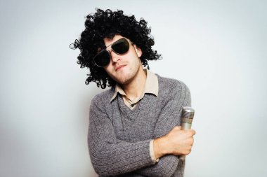 Peruklu ve güneş gözlüklü bir adam mikrofona şarkı söylüyor..