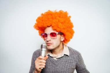 Peruklu ve güneş gözlüklü bir adam mikrofona şarkı söylüyor..