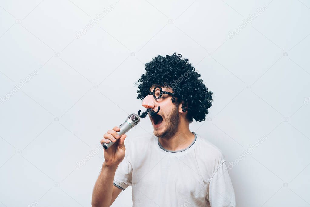 A man in a wig and funny glasses, singing into the microphone