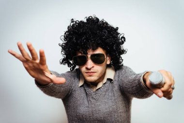 Peruklu ve güneş gözlüklü bir adam mikrofona şarkı söylüyor..