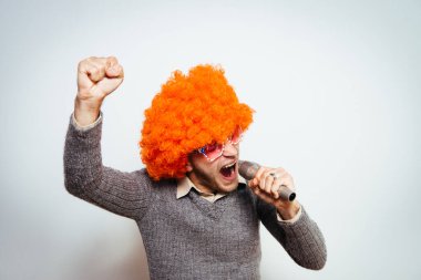 Peruklu ve güneş gözlüklü bir adam mikrofona şarkı söylüyor..