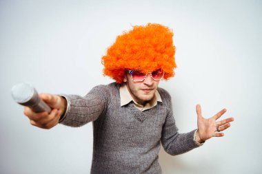 Peruklu ve güneş gözlüklü bir adam mikrofona şarkı söylüyor..