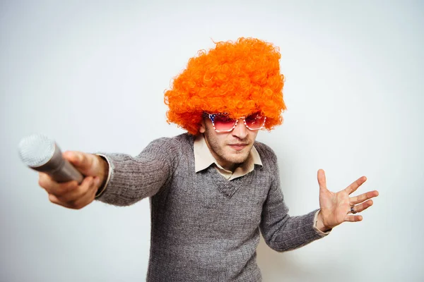 Peruklu ve güneş gözlüklü bir adam mikrofona şarkı söylüyor..