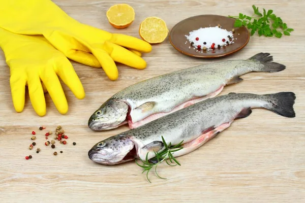Świeży pstrąg surowe ryby z przyprawami i gumowe rękawice do gotowania na drewnianym stole — Zdjęcie stockowe
