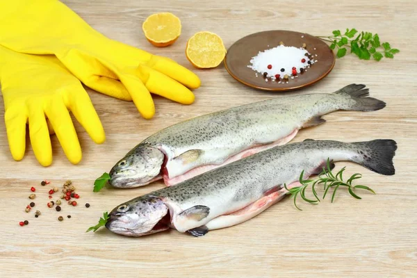 Świeży pstrąg surowe ryby z przyprawami i gumowe rękawice do gotowania na drewnianym stole — Zdjęcie stockowe