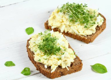 Bahçe tereli kahverengi ekmeğin üzerine yumurta salatası. Beyaz arka plan. Ev yapımı yumurta, mayonez ve hardaldan yapılmış..