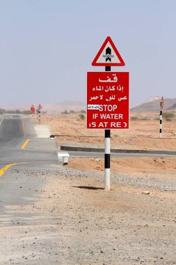 Yoldaki sellere karşı trafik işareti uyarısı, Umman. Issız dağların arasından geçen otoyol ve kırmızı uyarı işareti.  