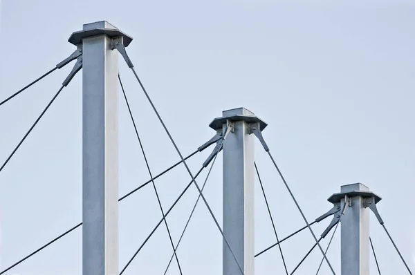 Gebundene Hängedachseile, drei hohe graue Masten, seilgefederte Pylon-Anker auf dem Dach, blassblauer Sommerhimmel, große, detaillierte horizontale Nahaufnahme, zeitgemäßes Baukonzept — Stockfoto
