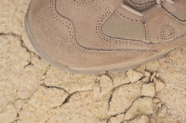 Brand new suede and nylon beige tan camo military tactical desert combat boot, arid dried soil and sand, detailed horizontal background macro close-up, bare earth, dust, pebbles, rough terrain off-road trekking, hiking concept — Stock Photo, Image