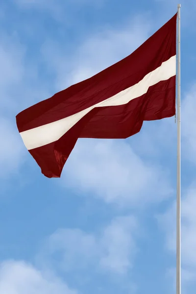 Republic of Latvia state flag, Latvian national carmine red vivid crimson and white bicolour ensign, official European Union, NATO member colours, large detailed vertical closeup, tall flagstaff flagpole mast pole post, blue summer sky cloudscape — 스톡 사진