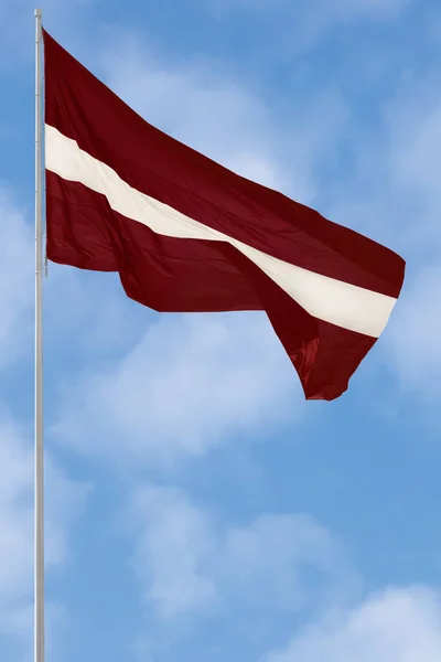 Republiken Lettland delstatsflagga, Lettlands nationalkarminröd levande crimson och vit tvåfärgad fänrik, Europeiska unionens officiella tidning, Nato-medlemsfärger, stor detaljerad vertikal närbild, hög flaggstav maststolpe, blå sommarhimmel — Stockfoto