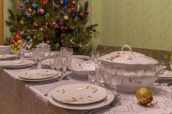 Mesa servida con vajilla festiva cerca de hermoso árbol de Navidad decorado en el interior del salón. Concepto de vacaciones de año nuevo en casa acogedora — Foto de Stock