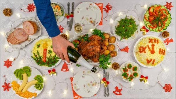 Die menschliche Hand hält eine Flasche Champagner und gießt Sekt ins Glas gegen den festlich gedeckten Weihnachtstisch. Abendessen für die Neujahrsparty, leckeres Essen. Feier Winterurlaub im gemütlichen Heim — Stockfoto