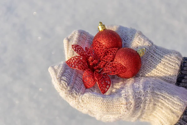 Ludzkie dłonie z otwartymi dłońmi w białych rękawiczkach z dzianin, trzymające ozdobne zabawki noworoczne na świeżym tle śniegu w słoneczny dzień. Wesołych Świąt i zimowych wakacji. Karta okolicznościowa z miejscem do kopiowania — Zdjęcie stockowe