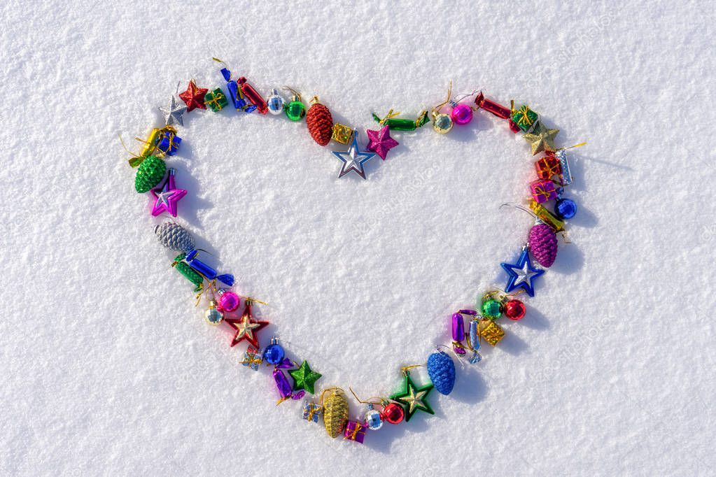 Heart symbol made of many colorful christmas or new year toys lying on white fresh snow in sunny winter day. Merry Christmas and Happy New Year. Winter holidays concept. Top view, copy space