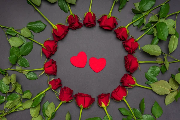 Dois corações vermelhos em armação redonda feita de flores de rosas frescas no fundo preto. Estilo moderno, composição criativa. Amor, romance, o conceito do Dia dos Namorados. Deitado plano, vista superior — Fotografia de Stock