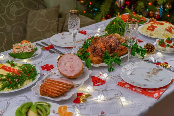 Святкове Різдво подається на стіл проти красивої зеленої сосни, прикрашеної багатьма барвистими новорічними іграшками. Різдвяна вечеря, смачна їжа, різдвяна індичка. Святкування зимових свят у затишному будинку — стокове фото