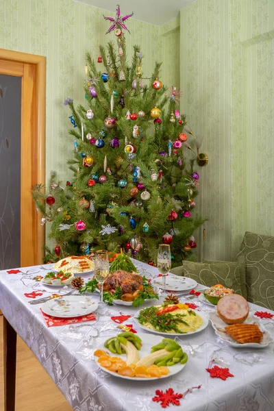 Navidad festiva sirvió mesa contra hermoso pino verde decorado con muchos juguetes coloridos de año nuevo. Cena de Navidad, comida deliciosa, pavo de Navidad. Celebración de las vacaciones de invierno en casa acogedora — Foto de Stock