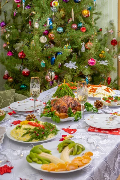 Navidad festiva sirvió mesa contra hermoso pino verde decorado con muchos juguetes coloridos de año nuevo. Cena de Navidad, comida deliciosa, pavo de Navidad. Celebración de las vacaciones de invierno en casa acogedora — Foto de Stock
