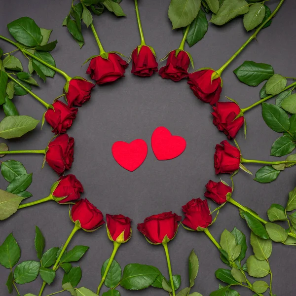 Dois corações vermelhos em armação redonda feita de flores de rosas frescas no fundo preto. Estilo moderno, composição criativa. Amor, romance, o conceito do Dia dos Namorados. Deitado plano, vista superior — Fotografia de Stock