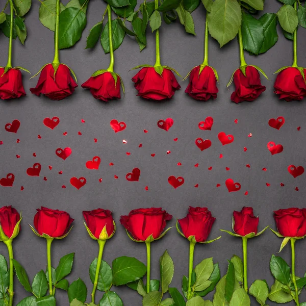 Кордон зроблений з свіжих червоних квіток троянд і серця конфетті на чорному тлі. Квіткова композиція, листівка на свято. Любовь, романтика или день Валентина. Вигляд зверху. — стокове фото