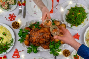 Köpüklü şarapla bardakları tutan insan elleri. Arkadaşlar ya da aile şenlikli Noel masasında şampanyayla kadeh kaldırıyor. Xmas yemeği, lezzetli yemekler, sıcacık evde kış tatili kutlaması.