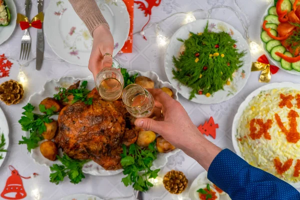 Human hands holding glasses with sparkling wine. Friends or family toasting with champagne over festive Christmas table. Xmas dinner, delicious food, winter holidays celebration at cozy home