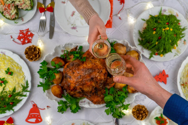 Human hands holding glasses with sparkling wine. Friends or family toasting with champagne over festive Christmas table. Xmas dinner, delicious food, winter holidays celebration at cozy home