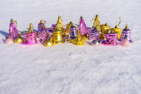 Conjunto de brinquedos de Natal em ouro e cores rosa deitado na neve branca fresca no dia ensolarado de inverno. Decorações de Ano Novo, cartão de saudação para férias de inverno. Feliz Natal e Feliz Ano Novo, espaço de cópia — Fotografia de Stock