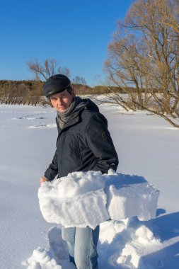 Güneşli bir günde ev sahasında kar temizleyen yakışıklı orta yaşlı beyaz bir adam. Kır evinden yola kürek döşeyen bir adam. Kış aktif eğlence kavramı