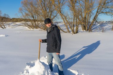 Güneşli bir günde ev sahasında kar temizleyen yakışıklı orta yaşlı beyaz bir adam. Kır evinden yola kürek döşeyen bir adam. Kış aktif eğlence kavramı