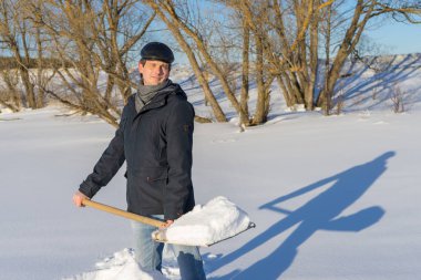 Güneşli bir günde ev sahasında kar temizleyen yakışıklı orta yaşlı beyaz bir adam. Kır evinden yola kürek döşeyen bir adam. Kış aktif eğlence kavramı