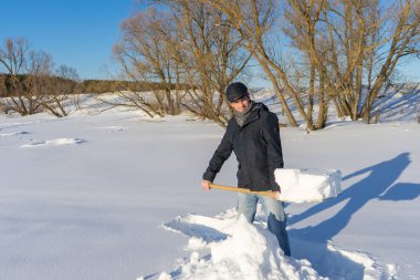 Güneşli bir günde ev sahasında kar temizleyen yakışıklı orta yaşlı beyaz bir adam. Kır evinden yola kürek döşeyen bir adam. Kış aktif eğlence kavramı