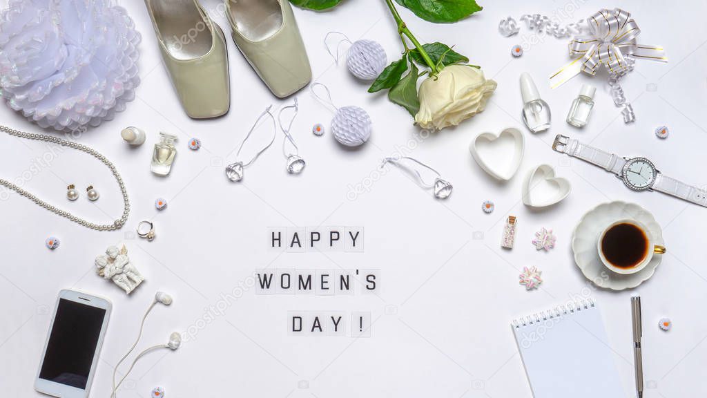 Text HAPPY WOMEN'S DAY. Stylish feminine accessories, decorative items, cosmetics, jewellery, hearts and rose flower on white background. Greeting card, flat lay, top view