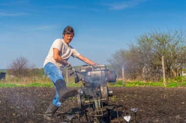Wellingtons 'da güneşli bir günde ekicisiyle toprağı süren bir adam. Banliyödeki mutfak-bahçe çiftçiliği. Toprak ekimi, toprak ekimi. Bahçede bahar işi. Bahçe konsepti.