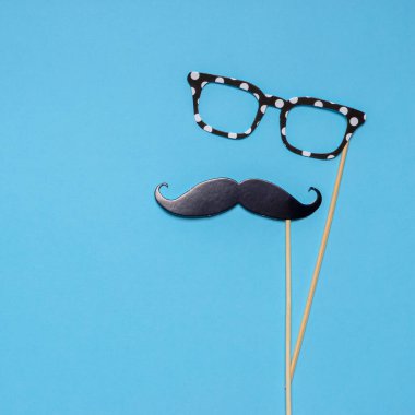 Fotoğraf kabini, mavi arka planda bıyık ve gözlük destekler. Babalar Günü için tebrik kartı ya da erkek sağlığı bilinçlendirme kampanyası konsepti. Düz konum, metin için boşluk.