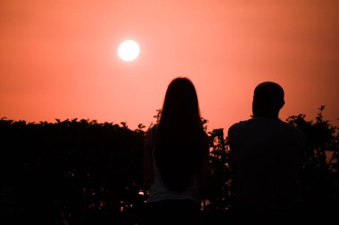 Aşık çift güzel bir kırmızı gün batımı karşılar.
