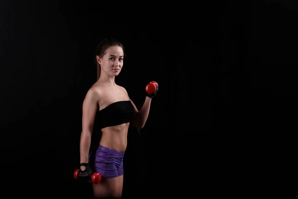 Deportiva chica sosteniendo una mancuerna sobre fondo negro . — Foto de Stock