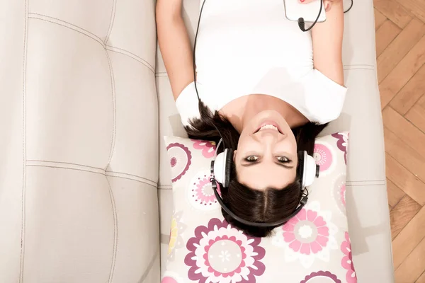 Schöne junge Frau, die auf der Couch liegt und Musik hört — Stockfoto