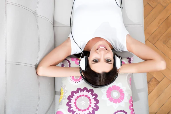 Hermosa joven acostada en el sofá escuchando música — Foto de Stock