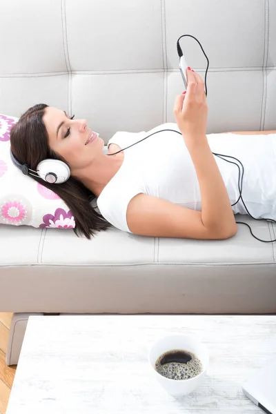Schöne junge Frau, die auf der Couch liegt und Musik hört — Stockfoto
