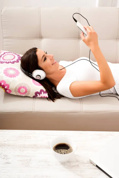 Gyönyörű fiatal nő fektetése a kanapéra, zenehallgatás — Stock Fotó