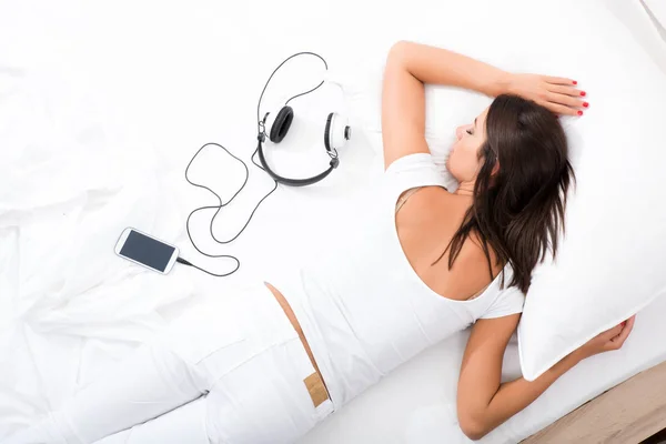Kadın bir akıllı telefon ve kulaklık ile yatakta döşeme — Stok fotoğraf