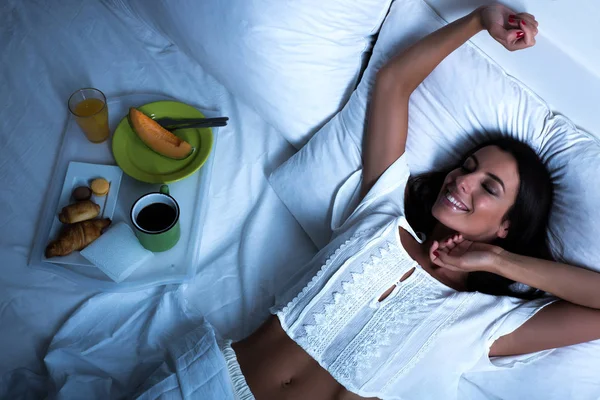 Mujer acostada en la cama con desayuno, y estiramiento — Foto de Stock