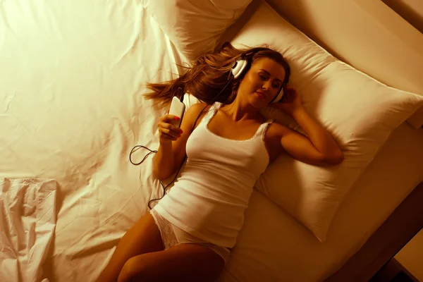 Hermosa mujer joven escuchando música por la noche en la cama —  Fotos de Stock